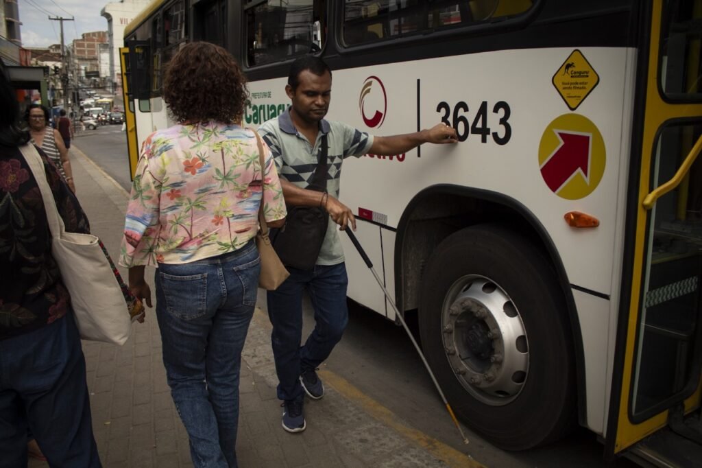 Luciano apoiando uma mão em um ônibus, enquanto procura o caminho com o auxílio de uma bengala